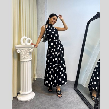 Woman in a black polka dot dress standing next to a white column and a large mirror.