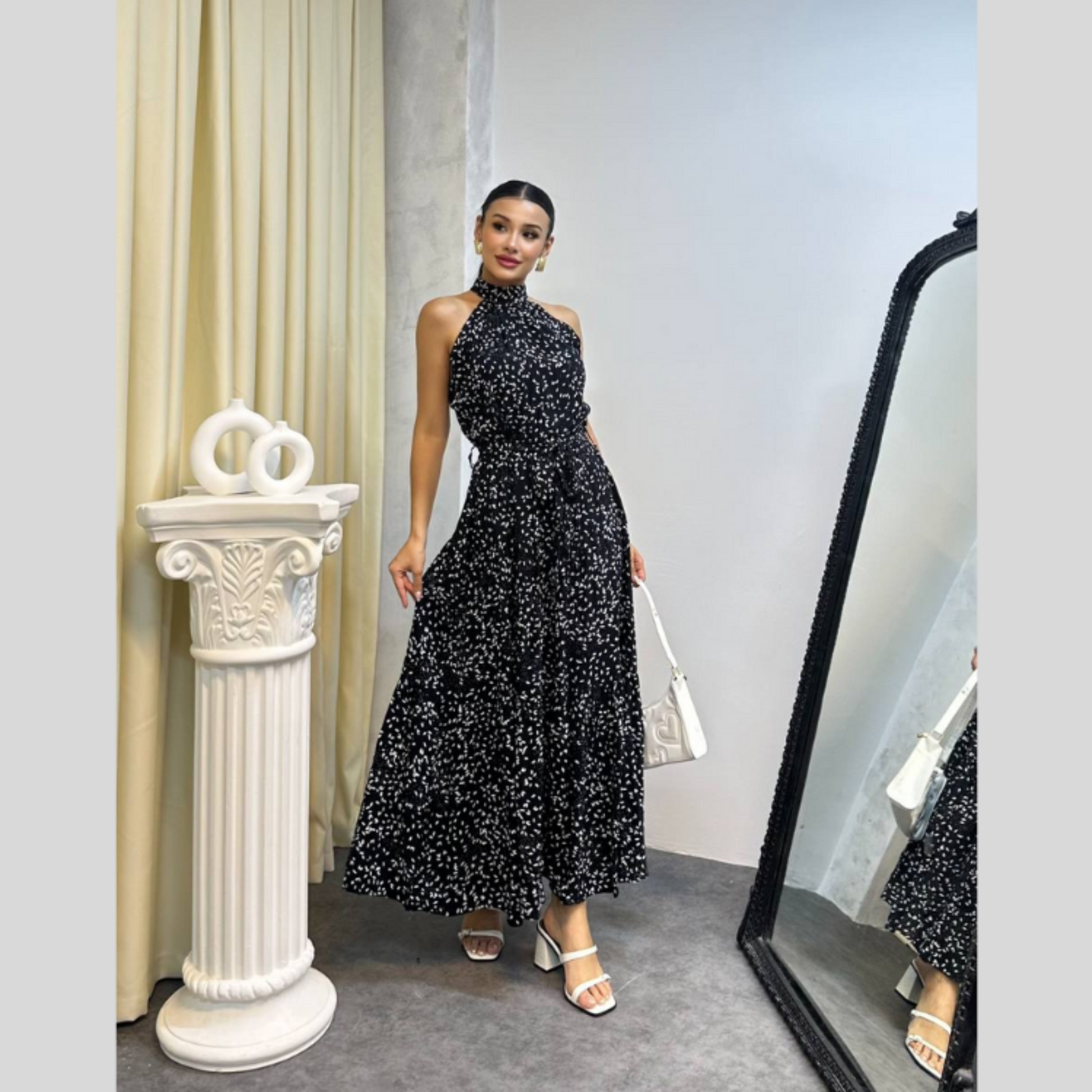 Woman in a black floral dress standing next to a white column in an indoor setting.