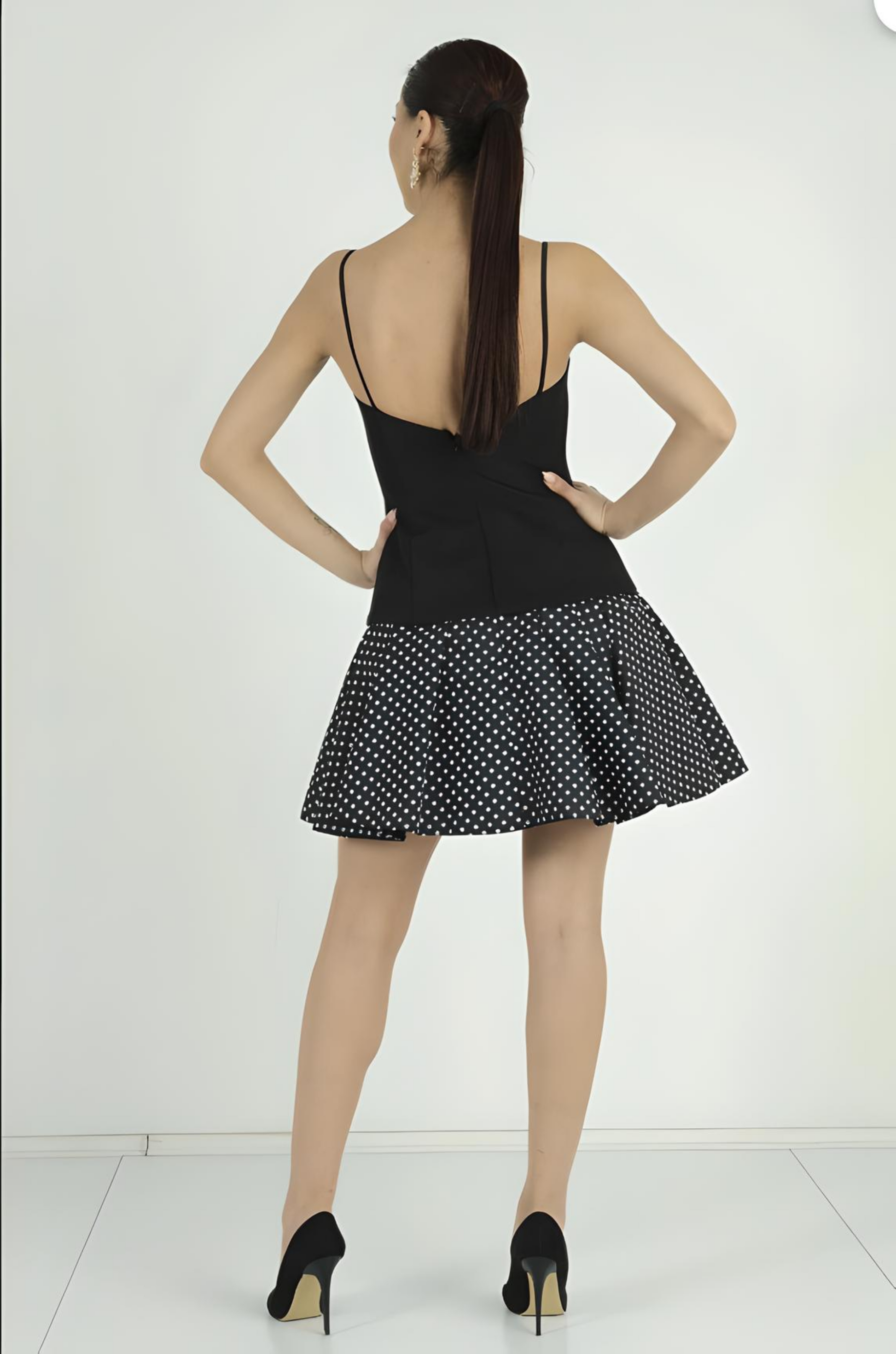 Woman wearing a black dress with a white polka dot pattern on a white background