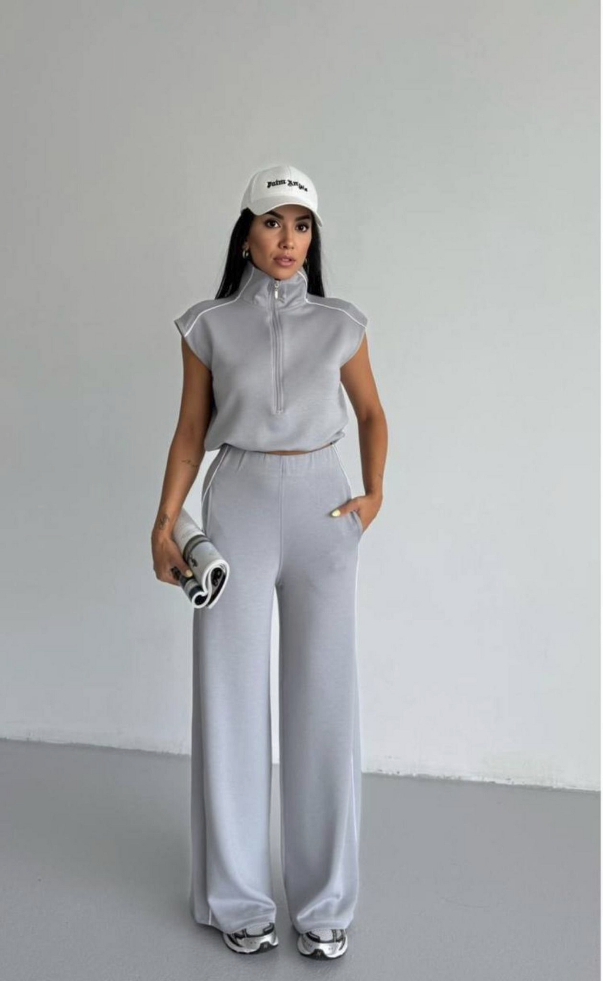 Woman in gray athletic outfit with white cap on a plain background