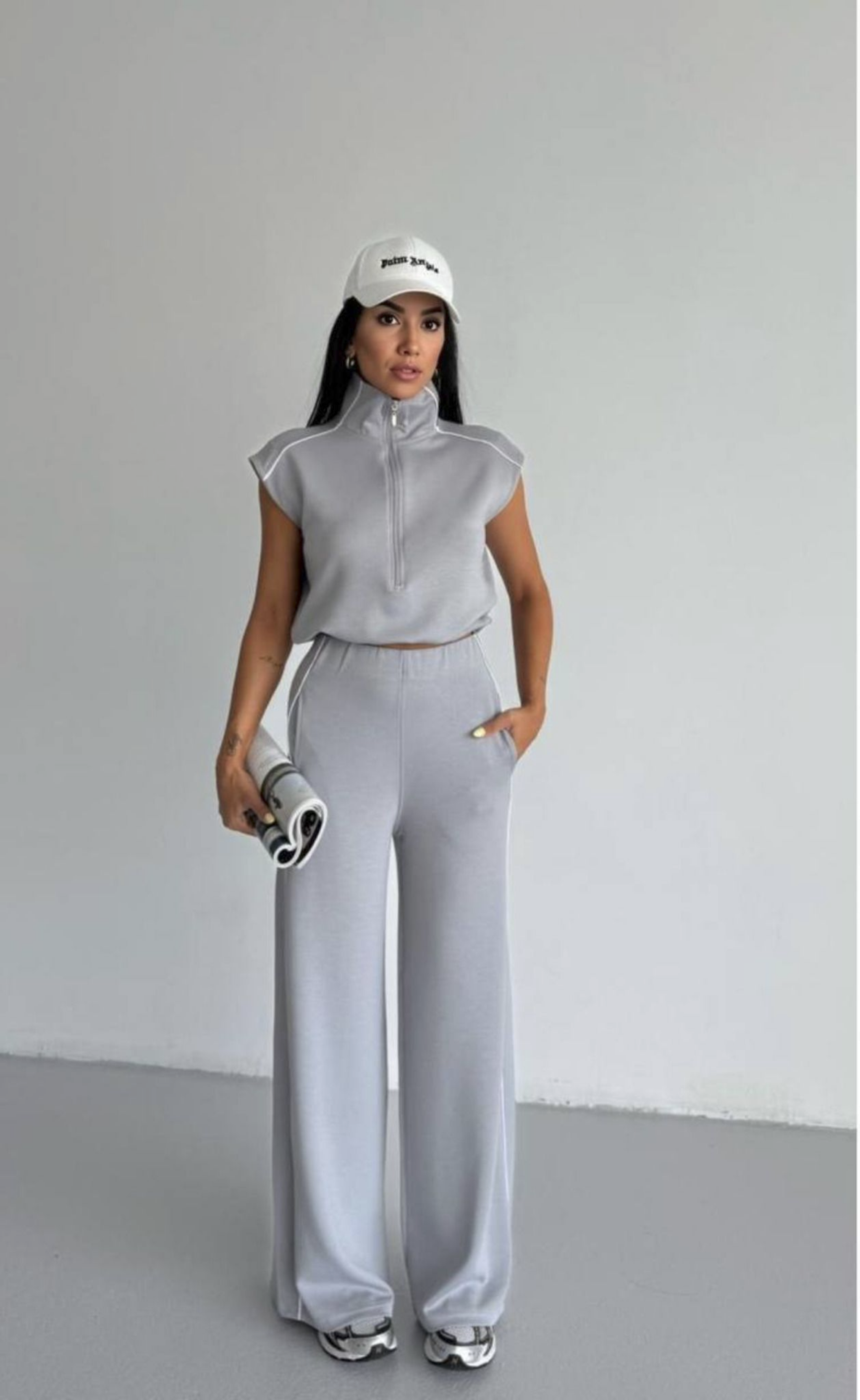 Woman in gray athletic outfit with white cap on a plain background