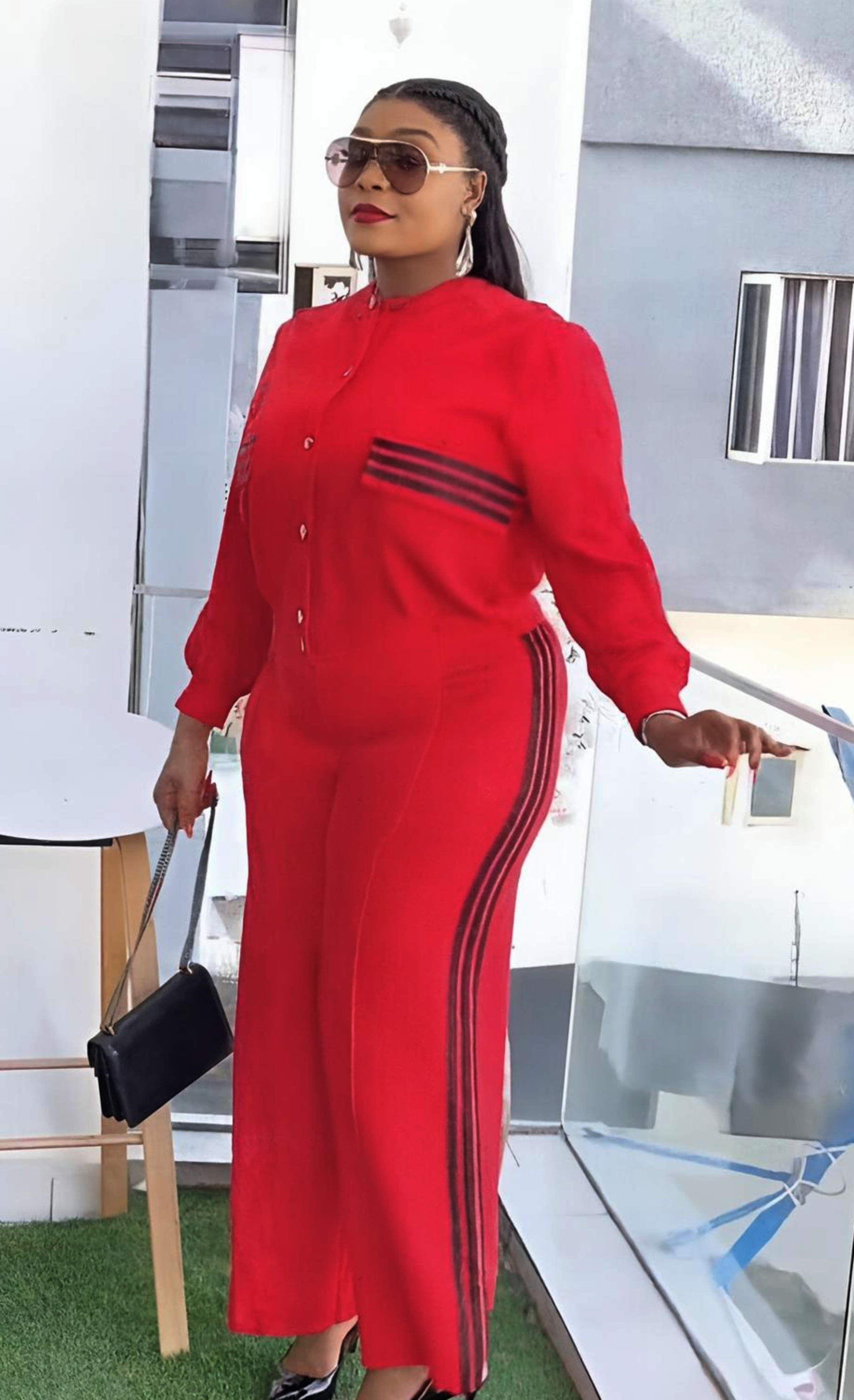 Woman in a red outfit with black stripes standing on a balcony.