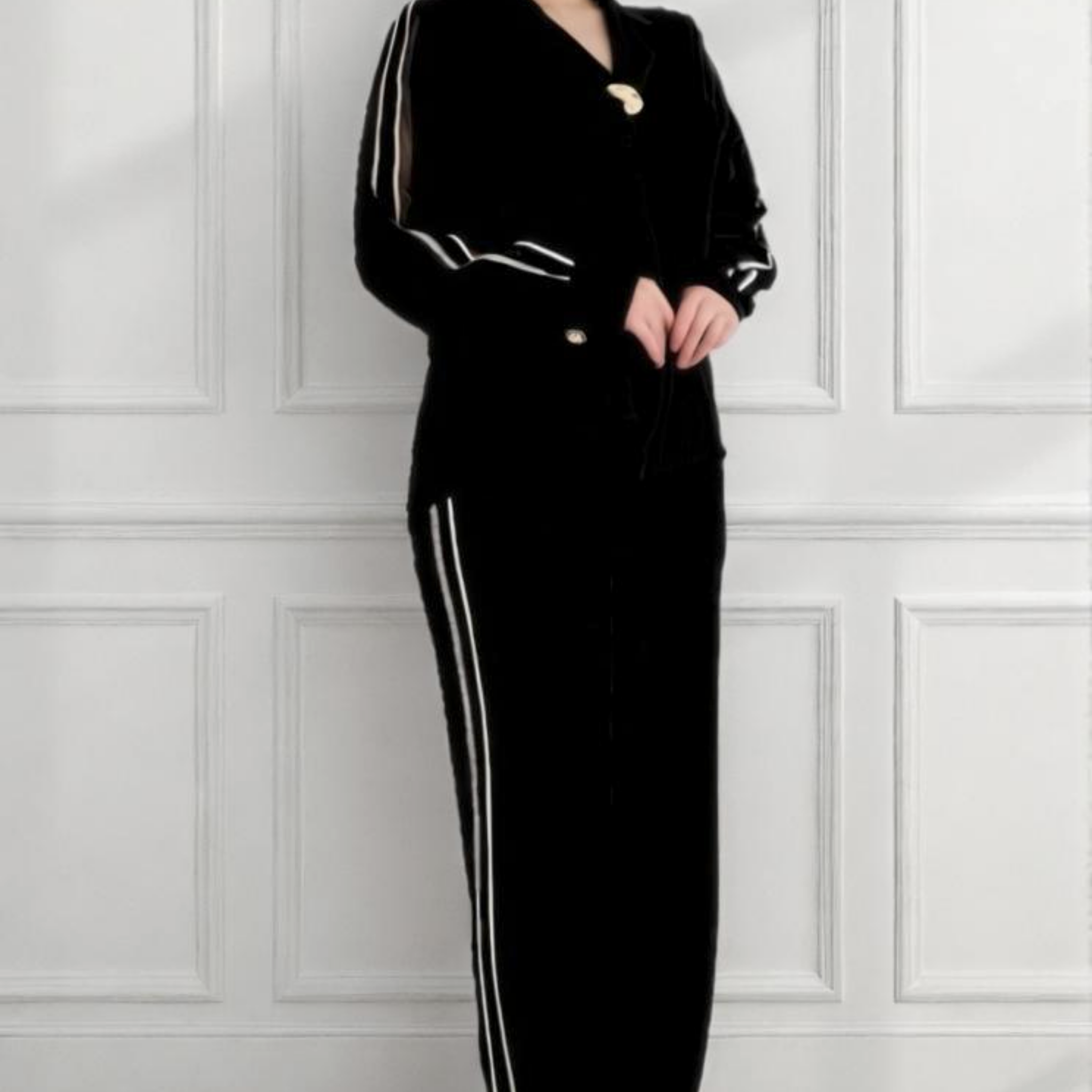 Woman wearing a black outfit with white stripes standing against a white paneled wall.