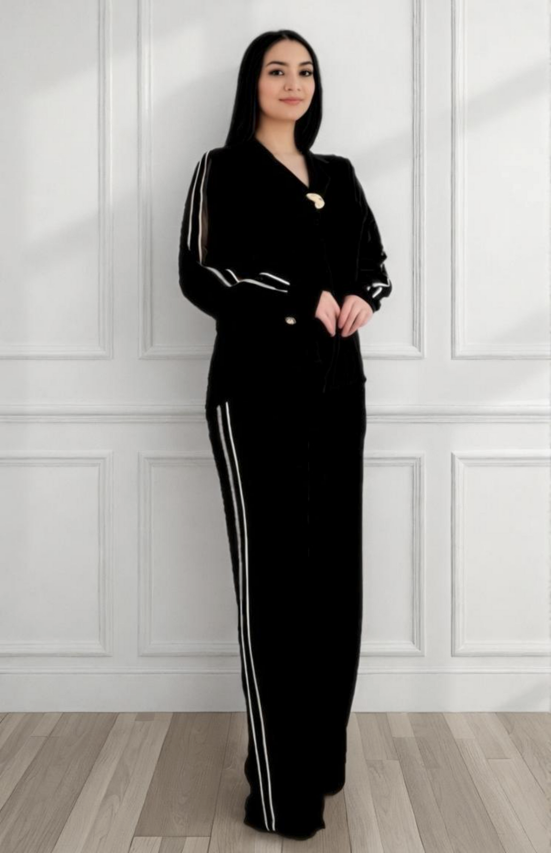Woman wearing a black outfit with white stripes standing against a white paneled wall.