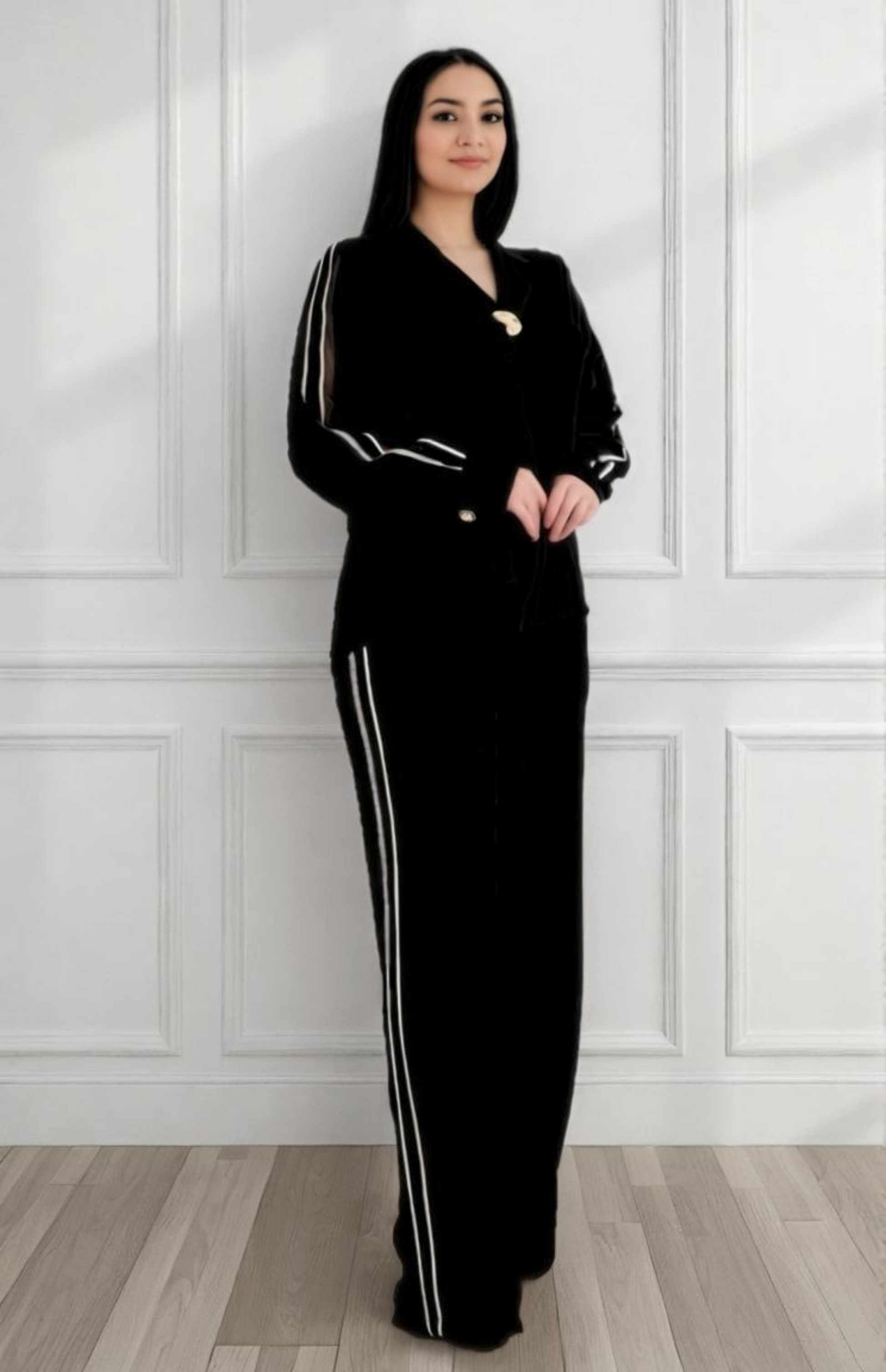 Woman wearing a black outfit with white stripes standing against a white paneled wall.