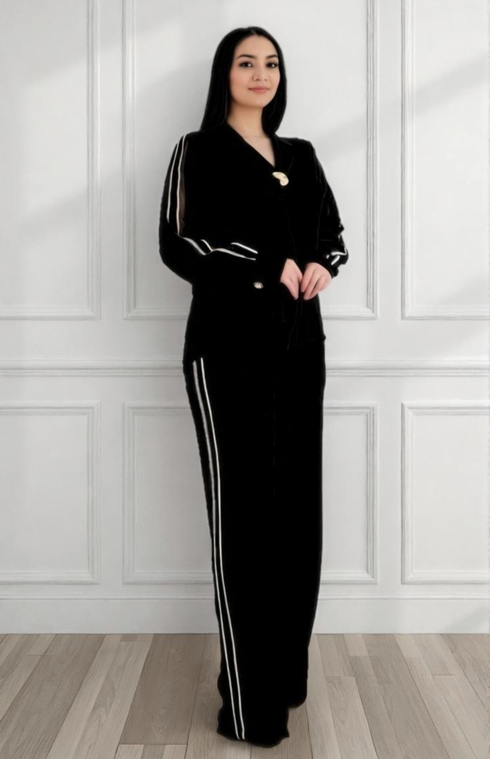 Woman wearing a black outfit with white stripes standing against a white paneled wall.