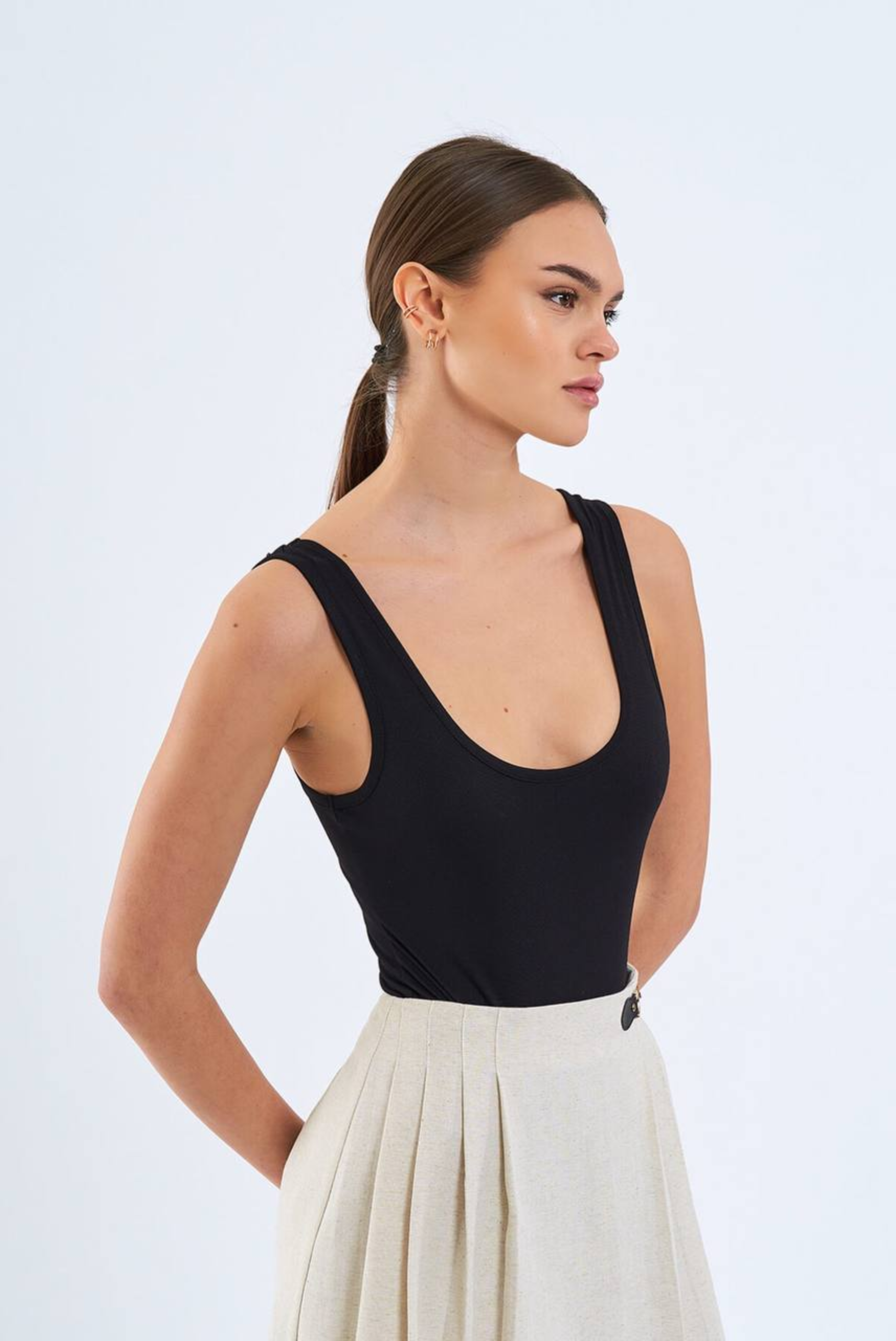 Woman wearing a black sleeveless top and white pants on a light gray background