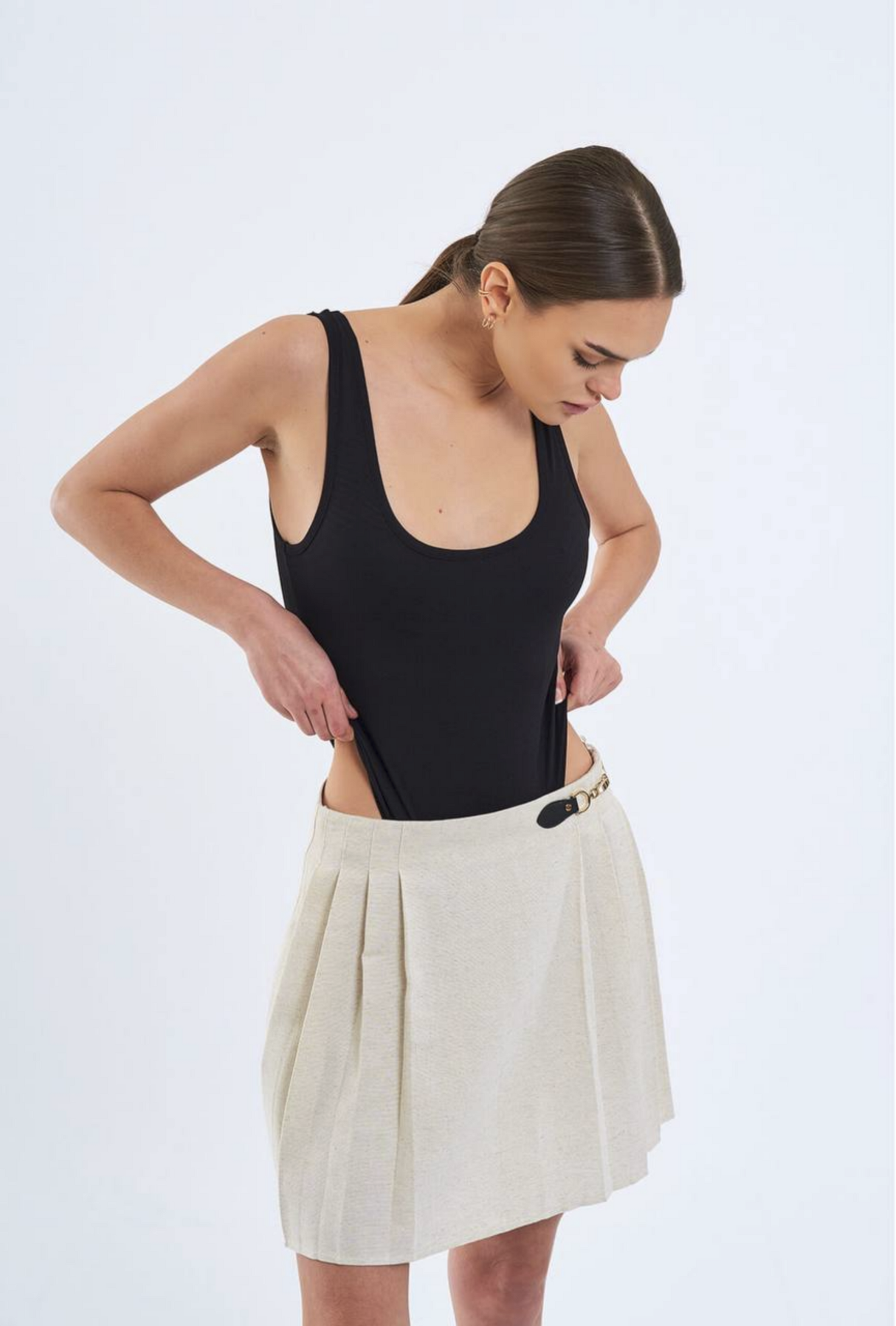 Woman wearing a black tank top and beige skirt on a light blue background