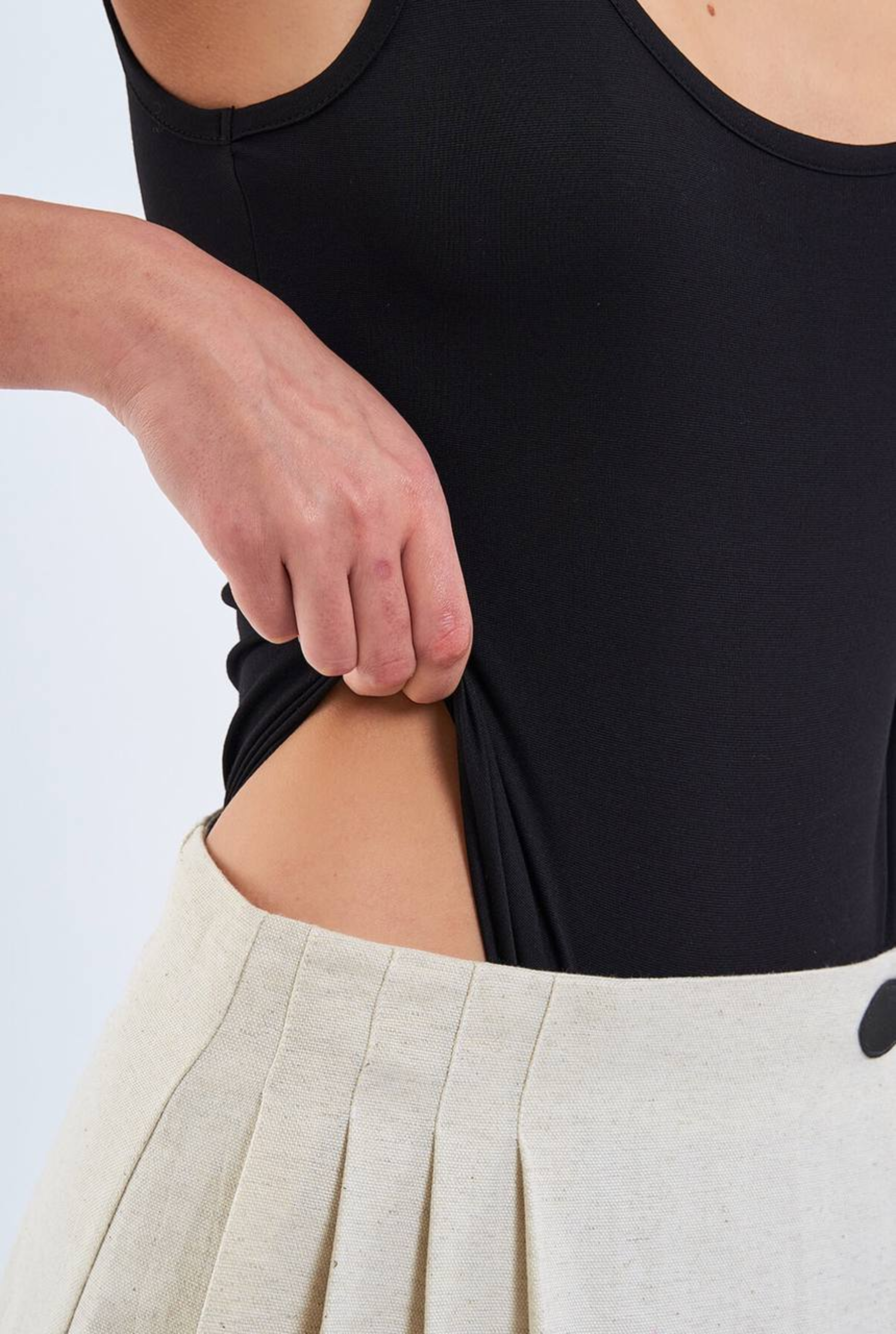 Person wearing a black tank top and beige pants on a light gray background