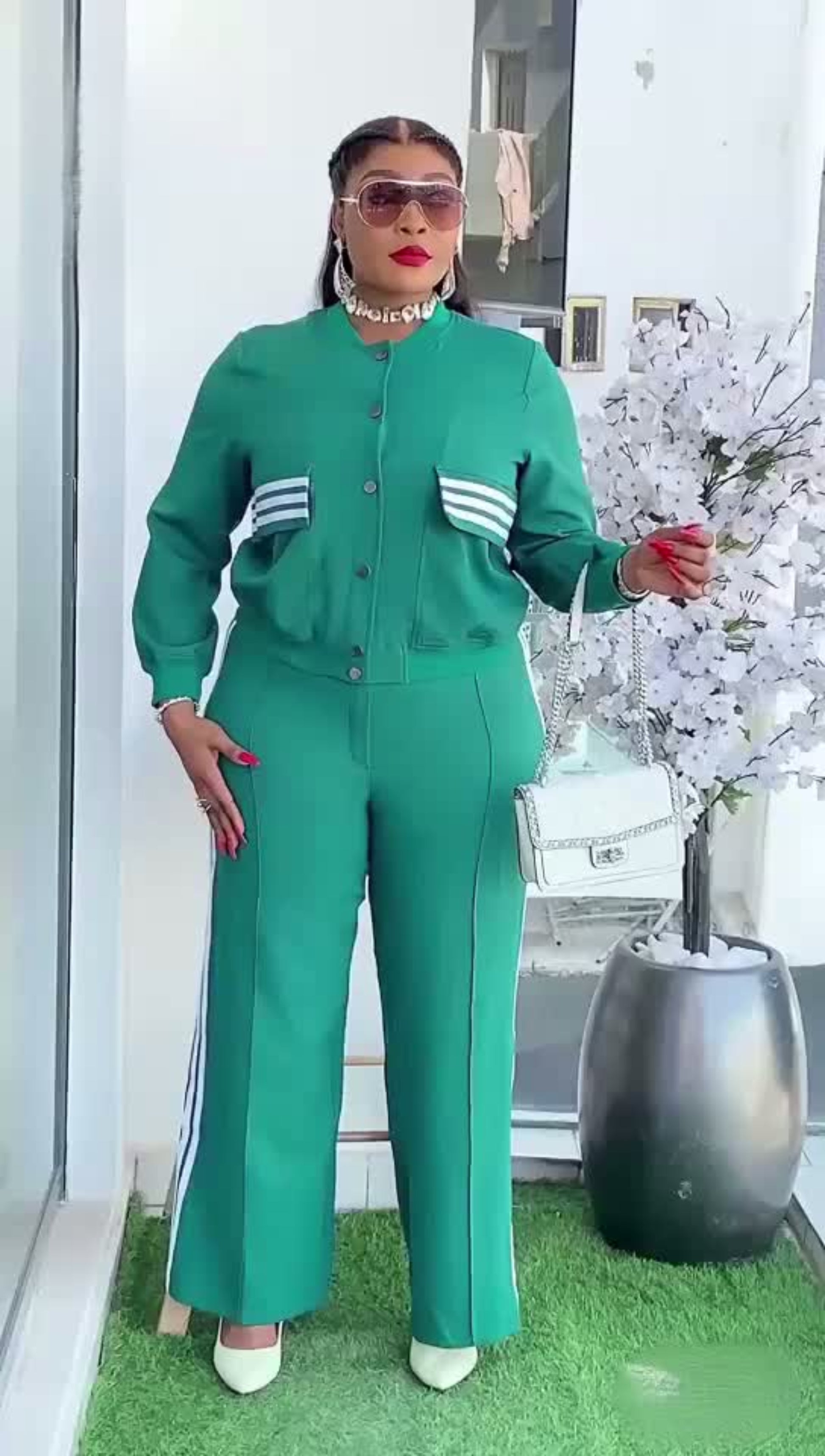 Woman in a green outfit standing outdoors with a white building and decorative elements in the background.