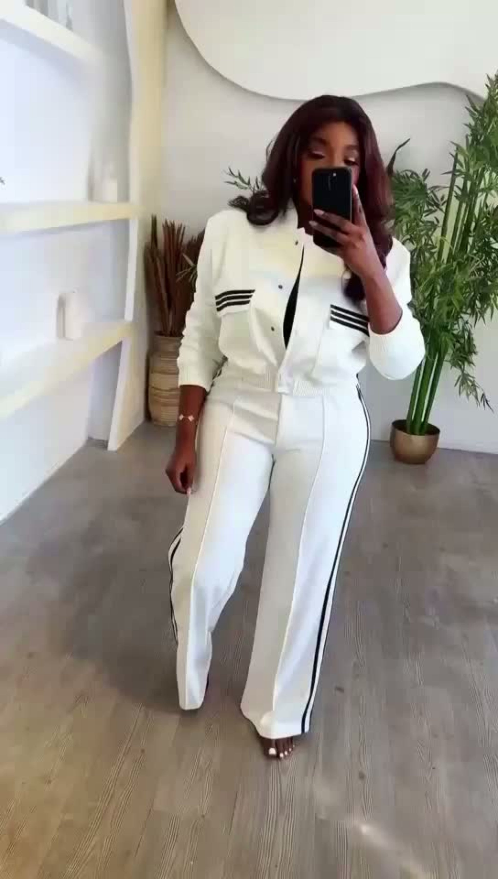 Person wearing a white outfit with black stripes in a minimalistic room.