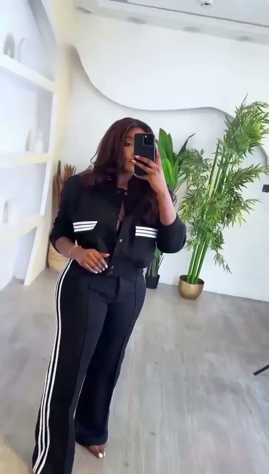 Person wearing a black tracksuit with white stripes in a room with plants.