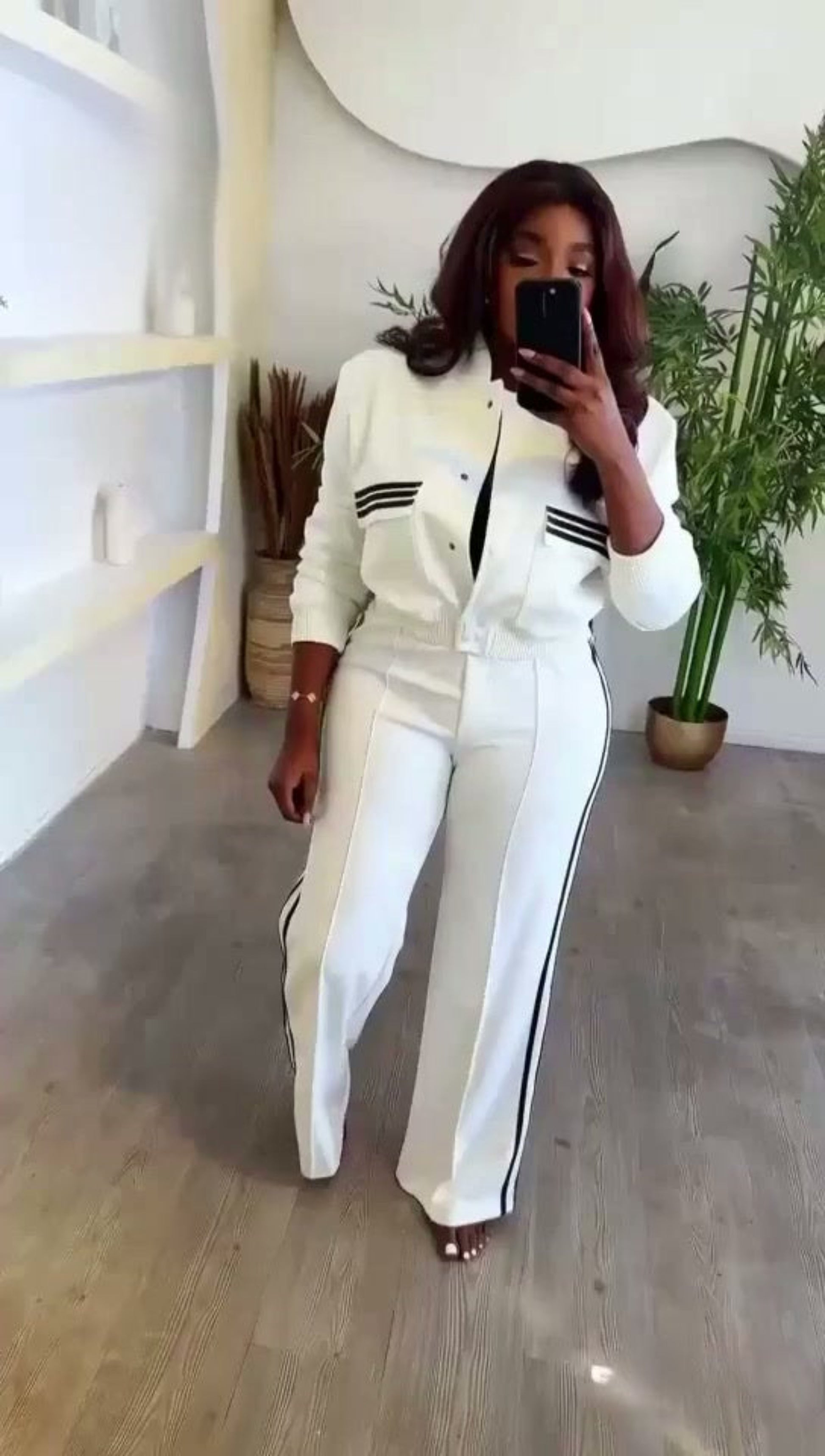 Person wearing a white outfit with black stripes in a minimalistic room.