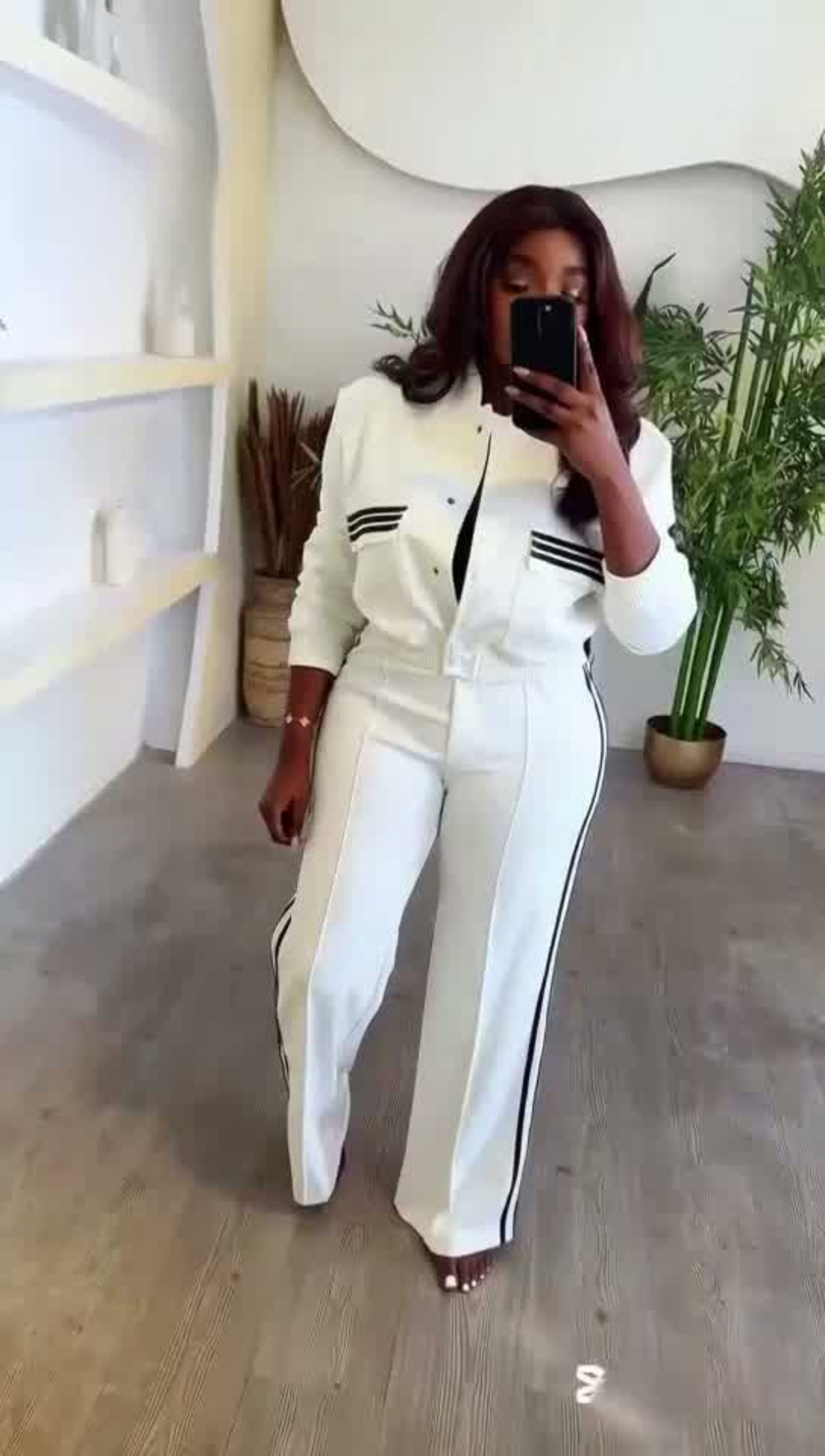 Person wearing a white outfit with black stripes in a minimalistic room.