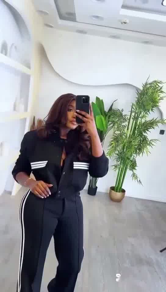 Person wearing a black tracksuit with white stripes in a modern indoor setting.