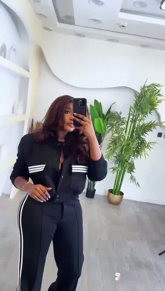 Person taking a mirror selfie wearing a black outfit with white stripes in an indoor setting.