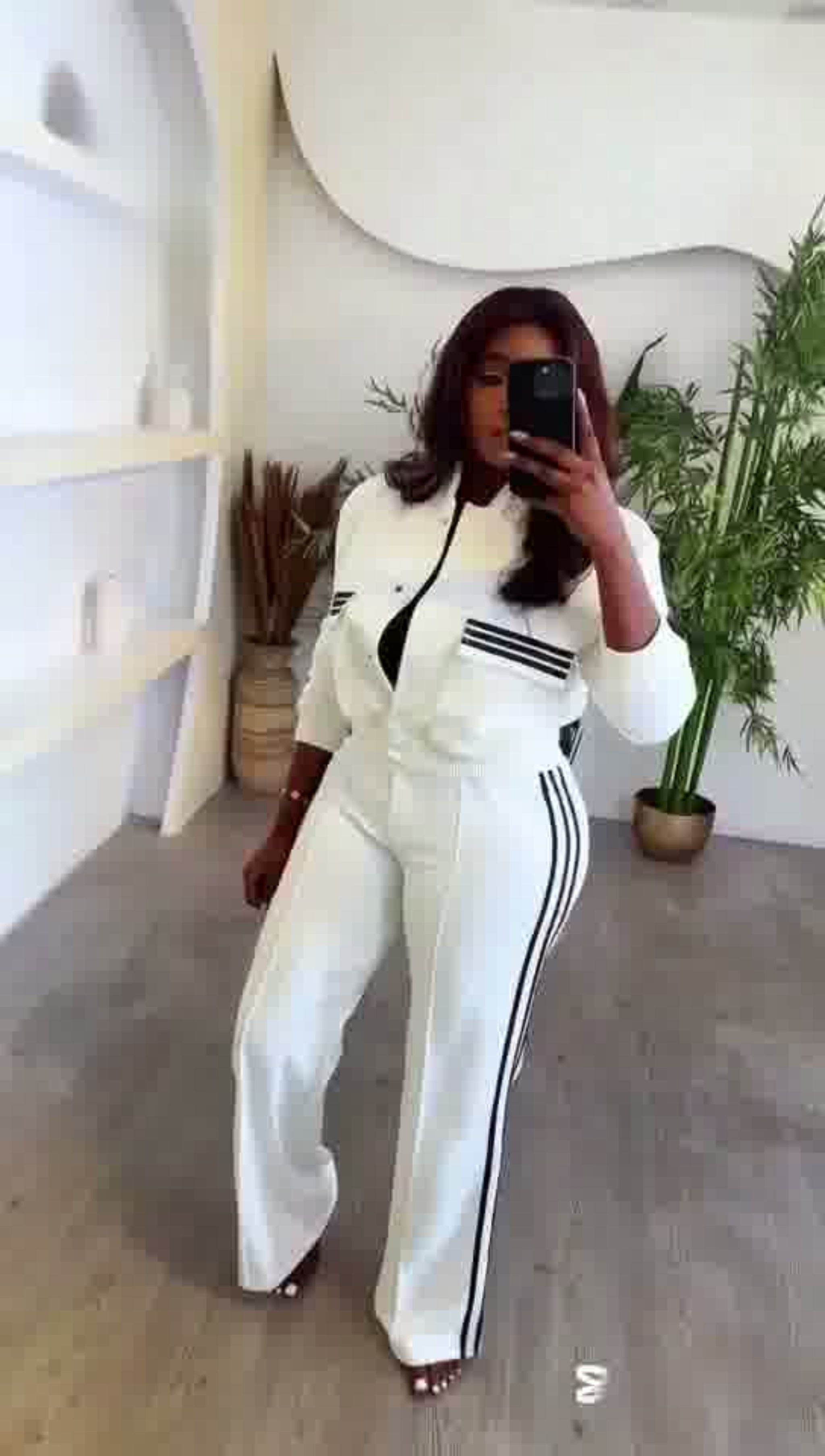 Person wearing a white tracksuit with black stripes in a minimalistic room.