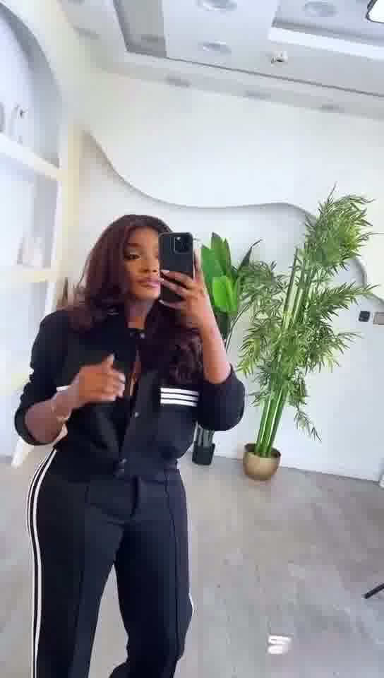 Person taking a mirror selfie wearing a black outfit with white stripes in a modern indoor setting.