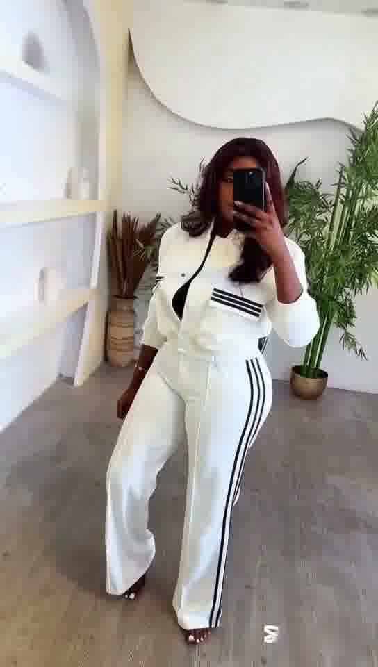 Person wearing a white outfit with black stripes in a minimalistic room.