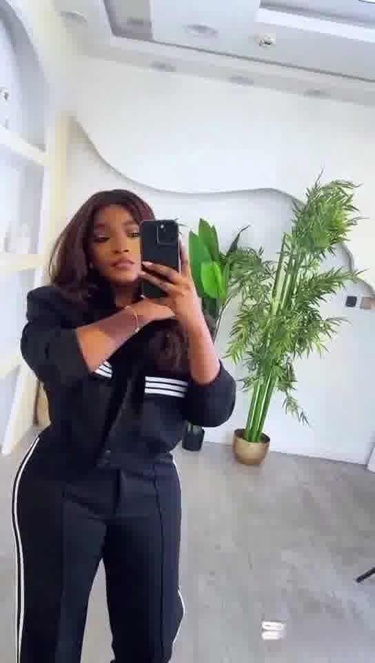 Person taking a mirror selfie wearing a black outfit with white stripes in a modern interior setting.