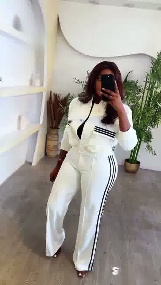 Person taking a mirror selfie wearing a white outfit with black stripes in a minimalistic room.