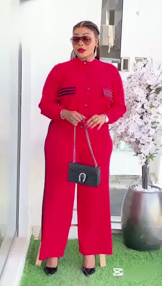 Woman in a red outfit standing outdoors with a plant and building in the background