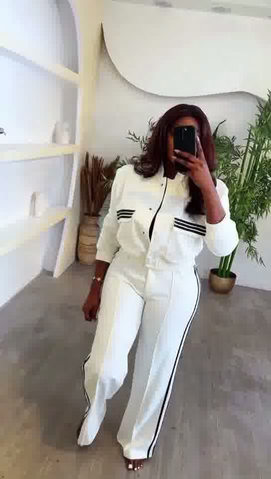 Person wearing a white outfit with black stripes in a minimalistic room.