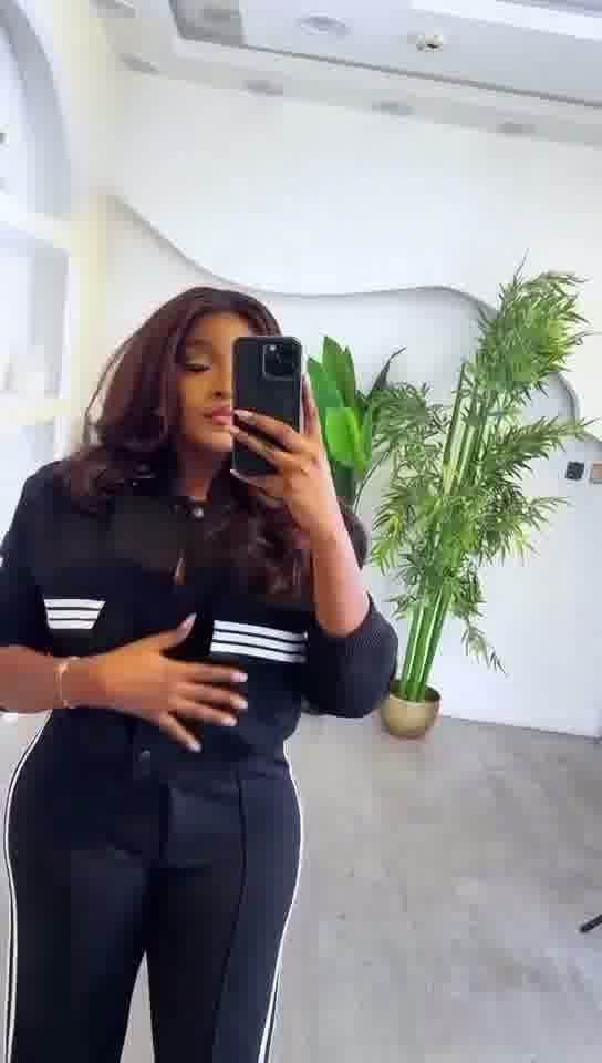 Person taking a mirror selfie wearing a black outfit with white stripes in a modern indoor setting.