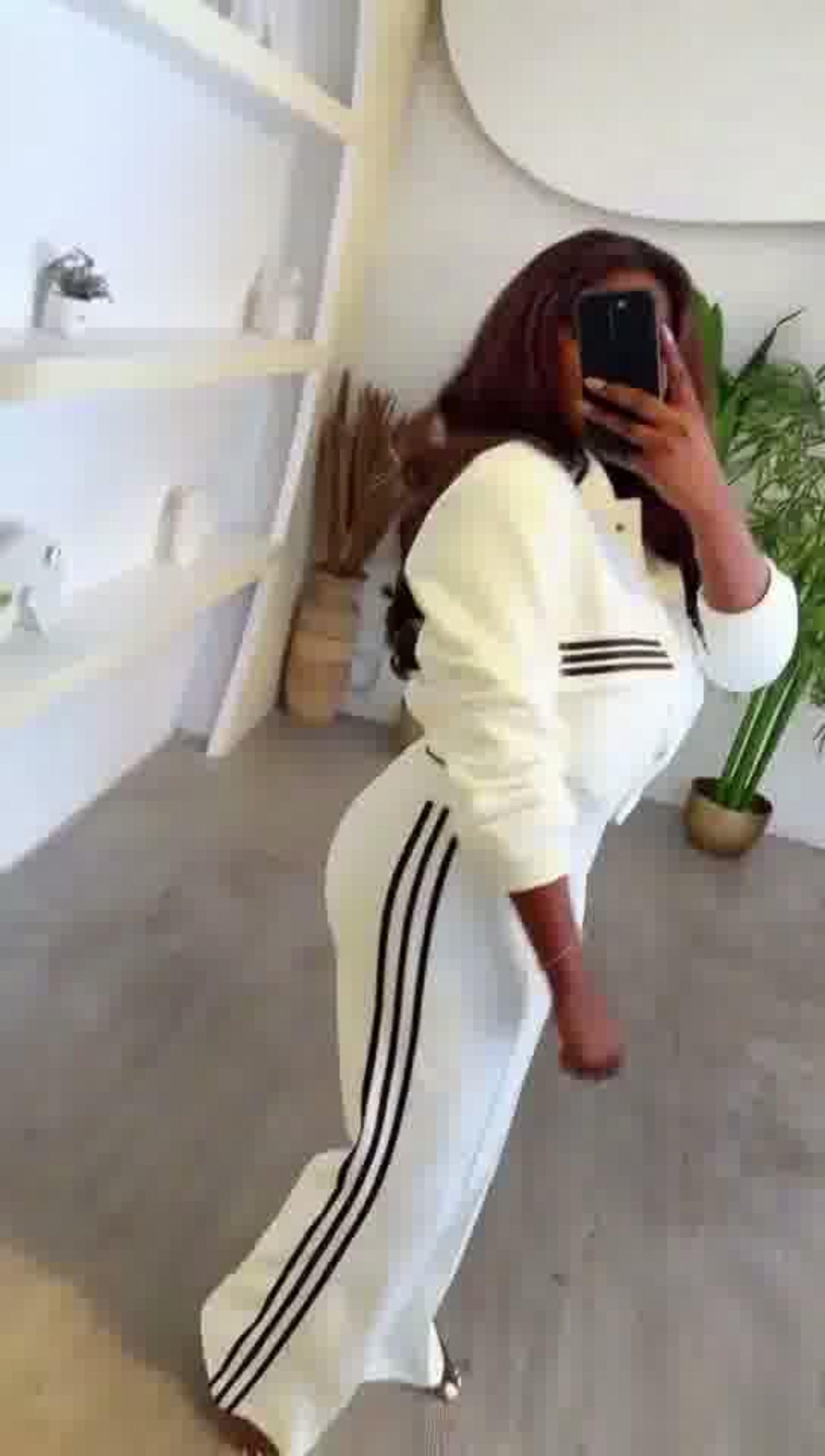 Person wearing a white outfit with black stripes in a room with a white wall and wooden floor.