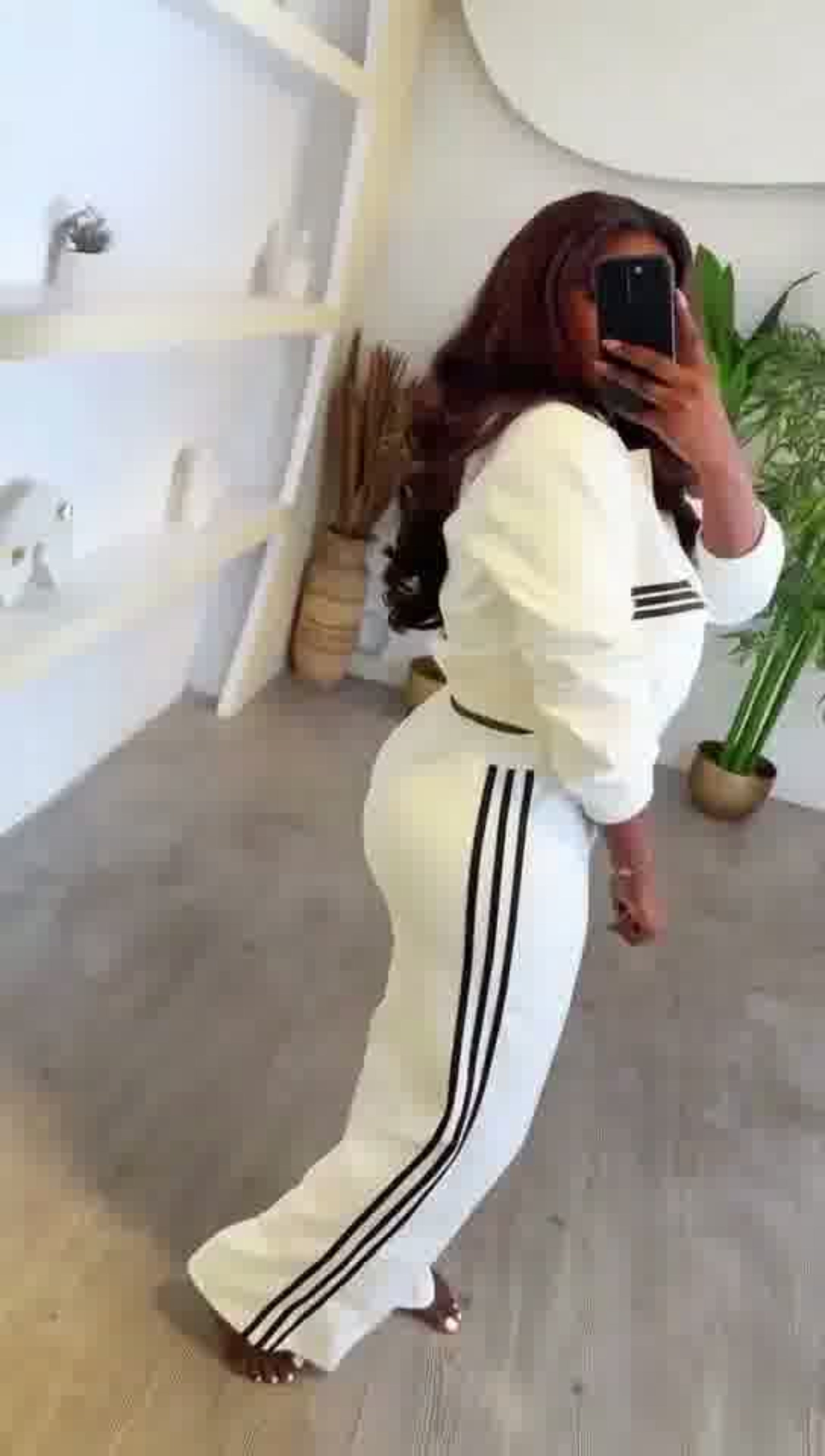 Person wearing a white tracksuit with black stripes in a room.