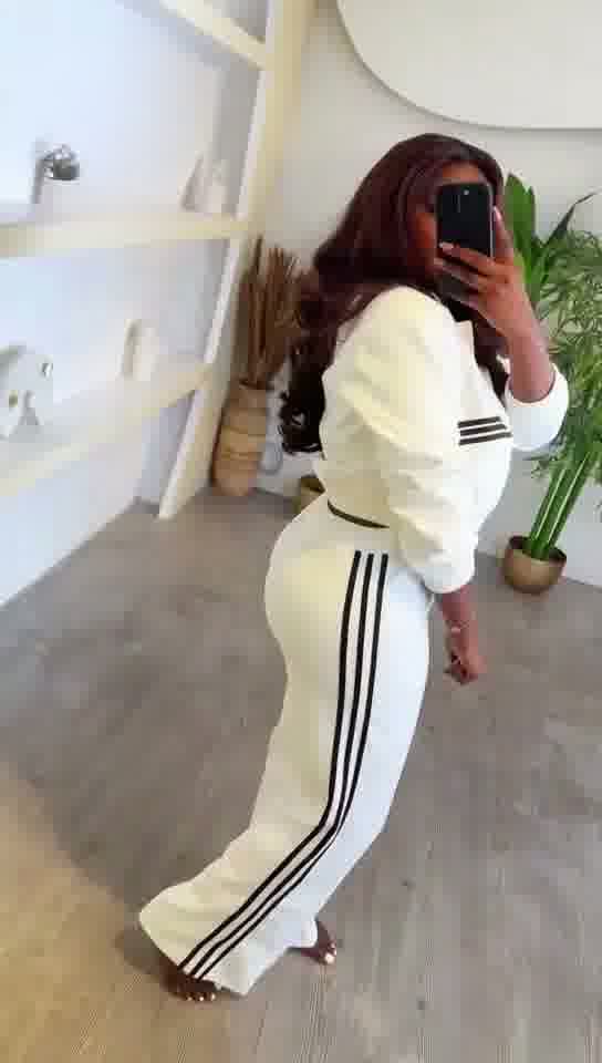 Person wearing a white outfit with black stripes in a minimal indoor setting