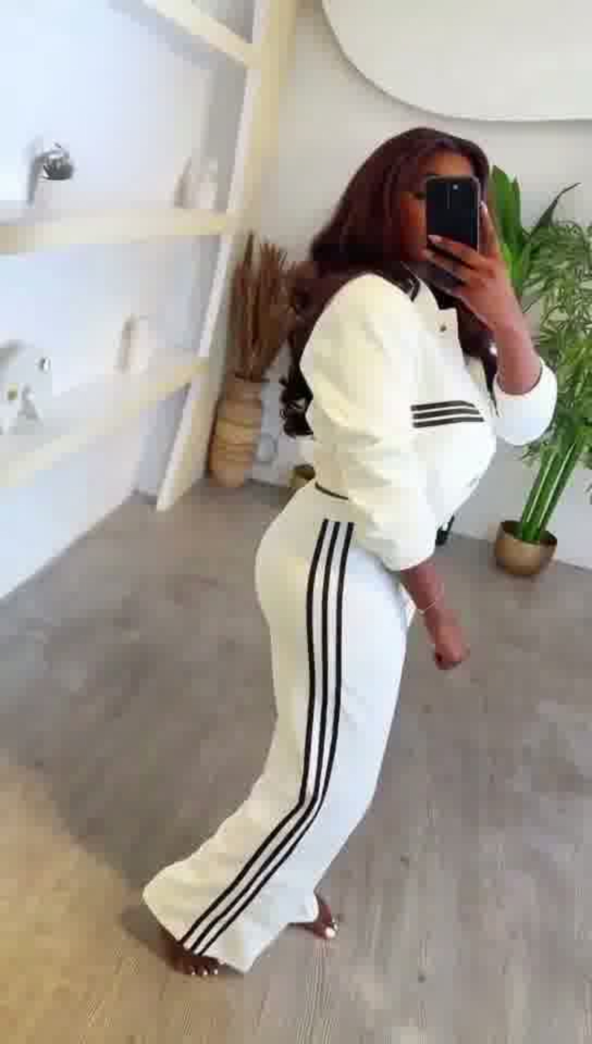 Person wearing a white tracksuit with black stripes in a room.