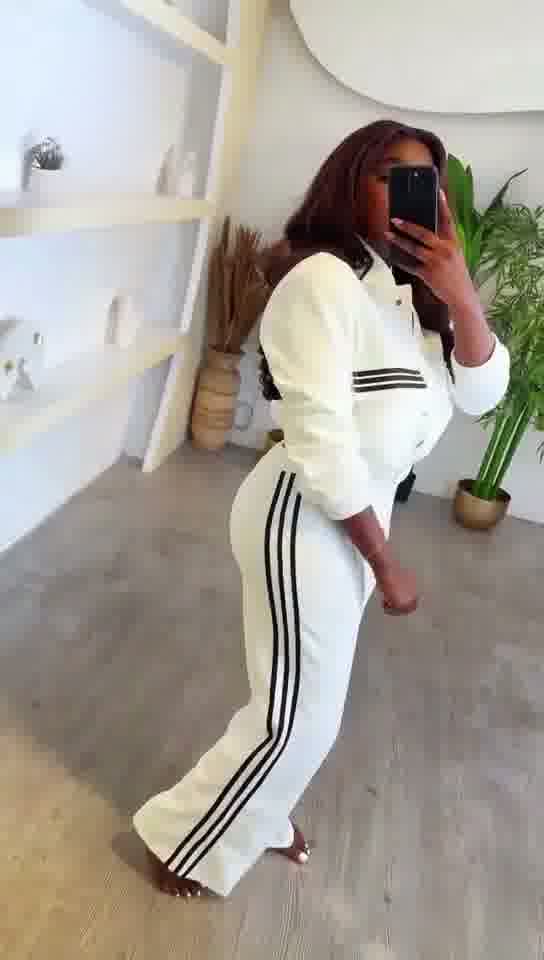 Person wearing a white tracksuit with black stripes in a minimalistic room.