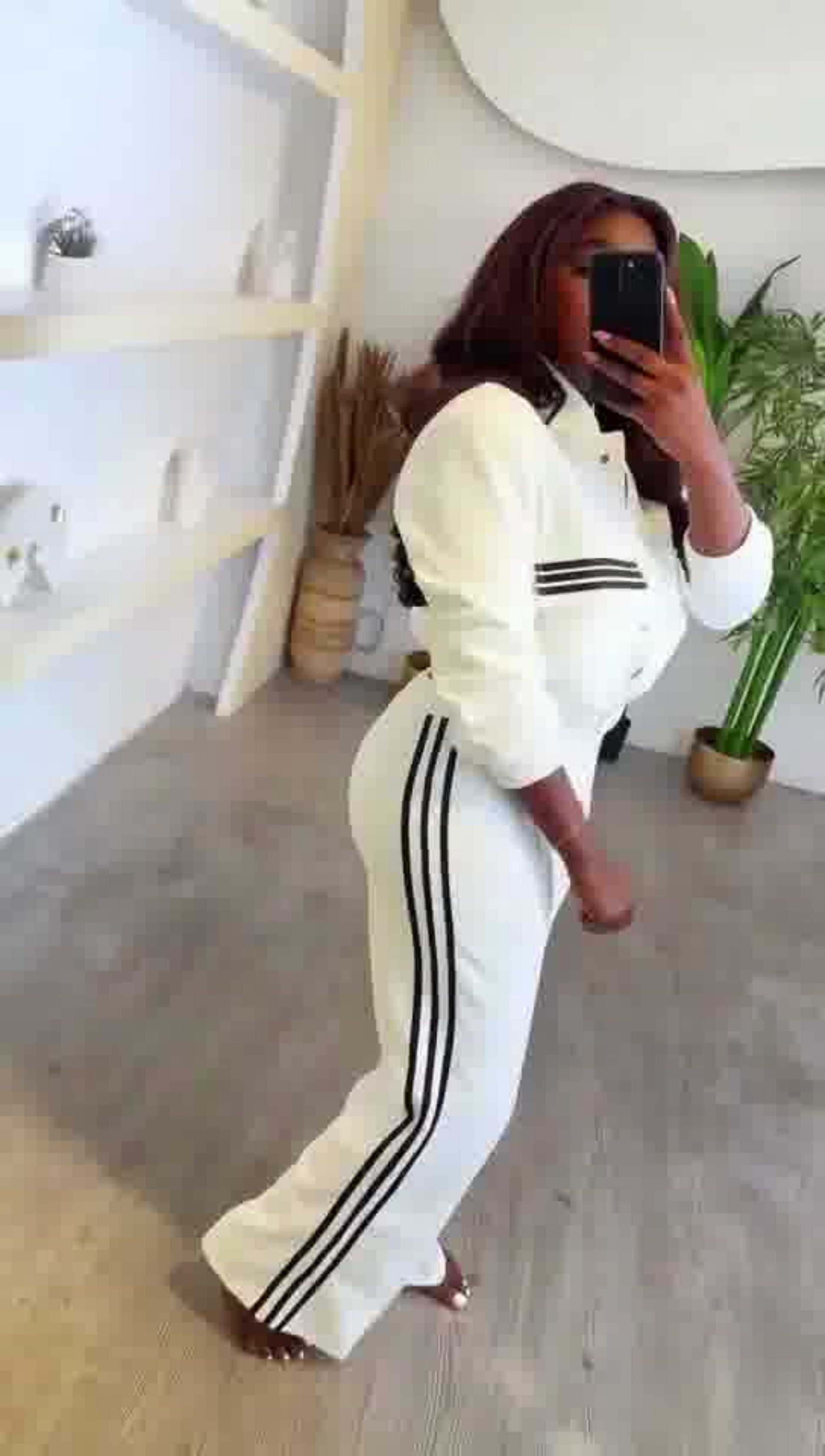 Person wearing a white tracksuit with black stripes in a minimalistic room.