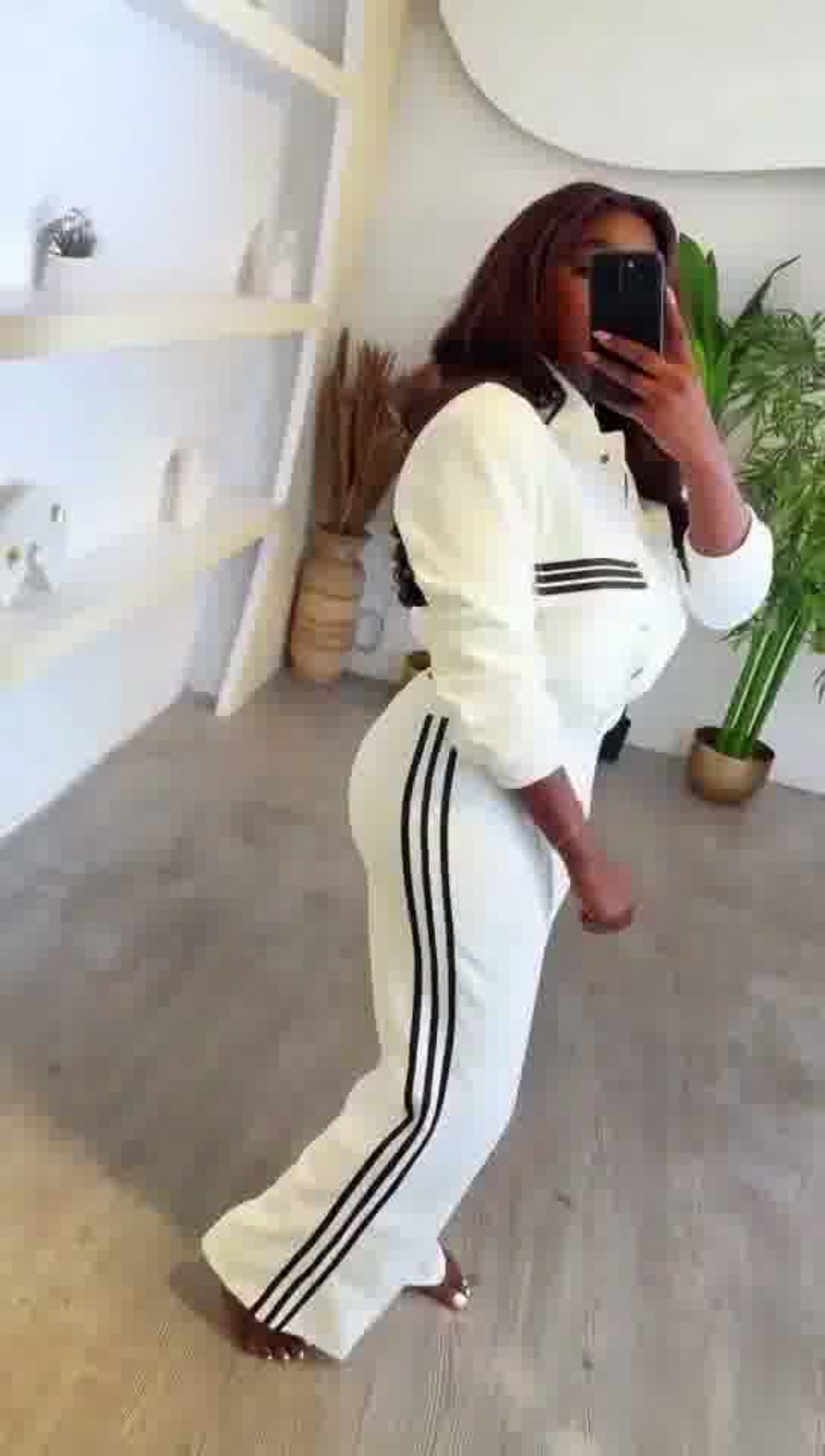 Person wearing a white tracksuit with black stripes in a minimalistic room.