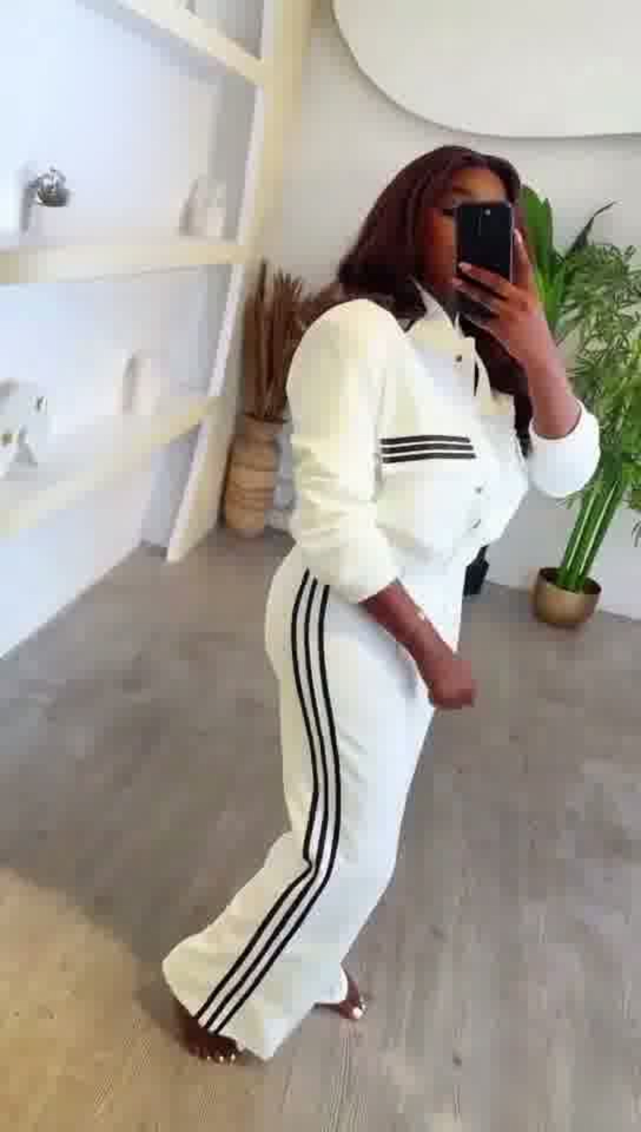 Person wearing a white tracksuit with black stripes in a room.