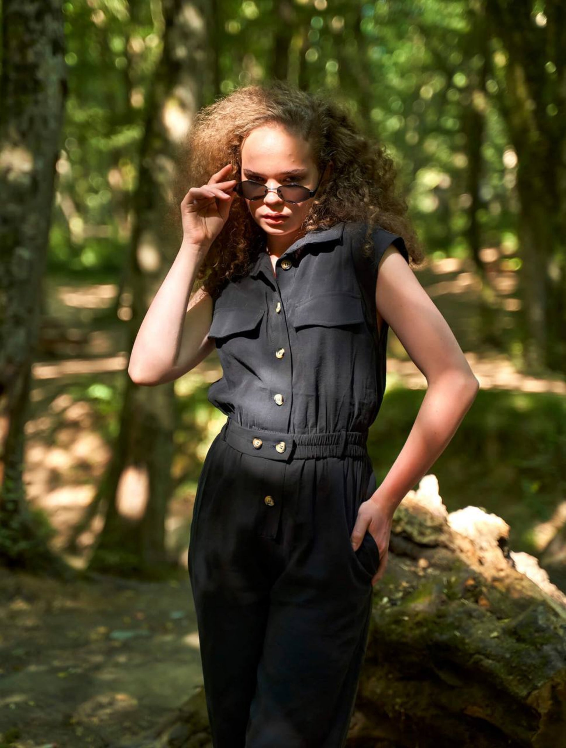 Person wearing a black sleeveless jumpsuit in a forest setting